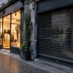 Créations et faillites d'entreprises : rue commerçante belge avec une vitrine neuve éclairée d'un côté et une vitrine fermée de l'autre